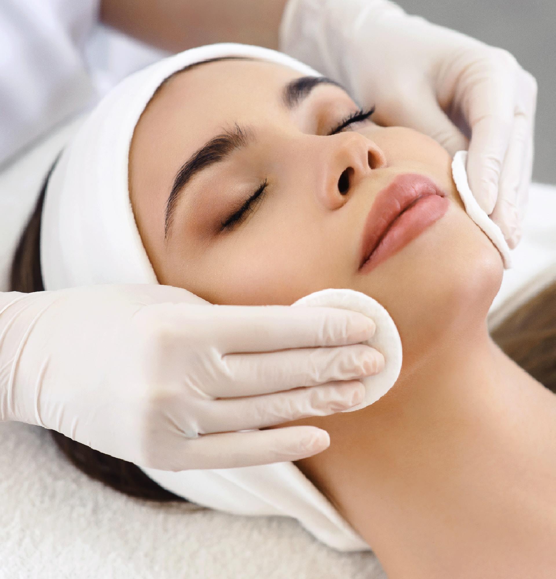 Close up of hands of skillful beautician cleaning and touching female face with cotton pad or sponge. The woman is lying and relaxing. Her eyes are closed with pleasure Institut de beauté à Gretz-Armainvilliers